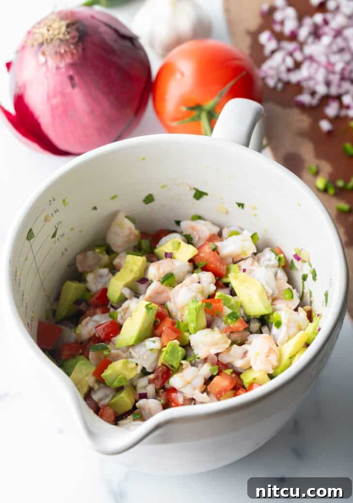 A white bowl showcasing the exquisite combination of succulent shrimp, creamy diced avocado, vibrant green and red peppers, and fresh cilantro, all mixed together to form the ceviche.