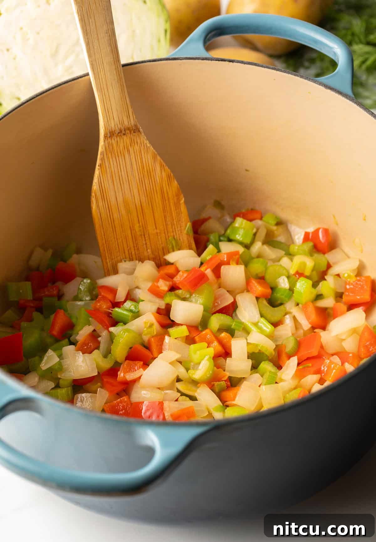 Comforting Ham and Cabbage Pot 4 Cooking diced onion, carrots, bell pepper and celery in a large blue cooking pot.