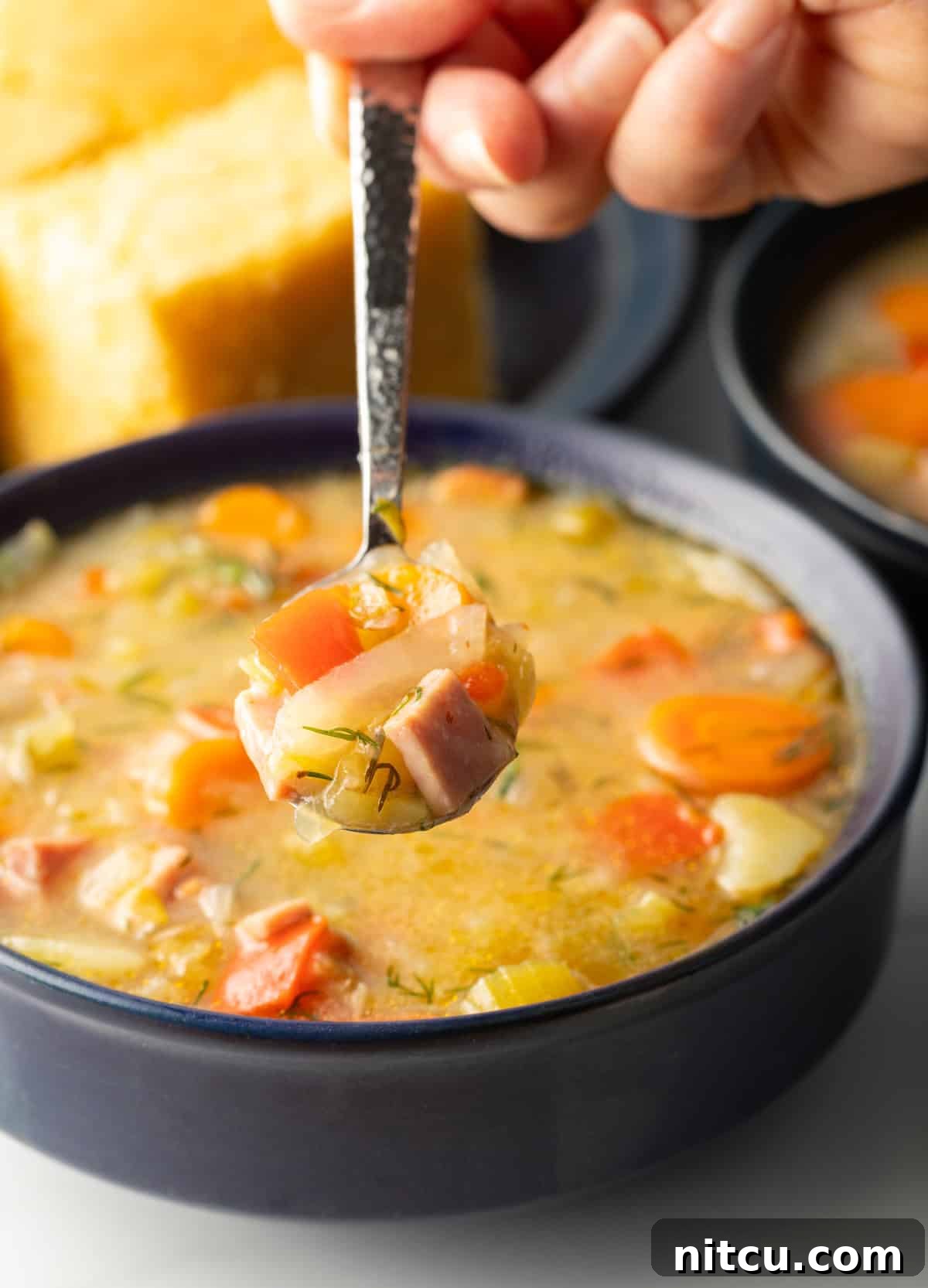 Comforting Ham and Cabbage Pot 7 Spoonful of soup held over black bowl of cabbage and ham soup, showing to camera.