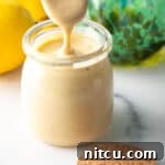 A spoon of creamy tahini dressing being held above a jar of tahini dressing, ready to be served.