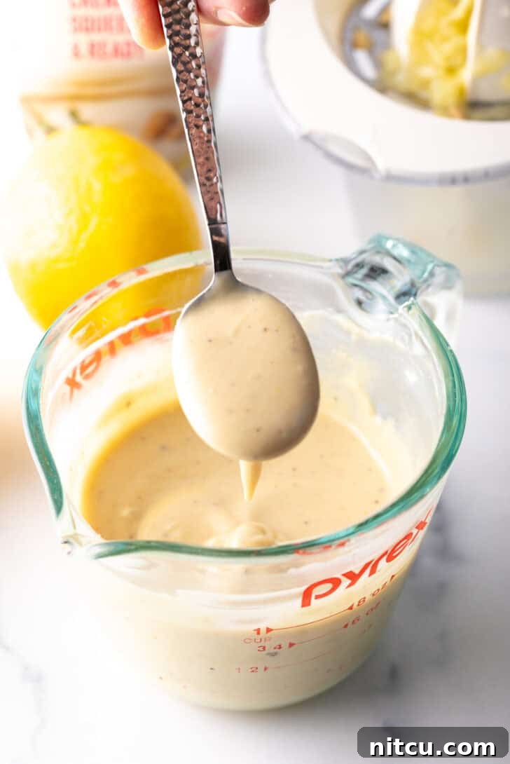 A spoonful of smooth, creamy tahini dressing held above a glass measuring cup filled with the freshly made dressing.