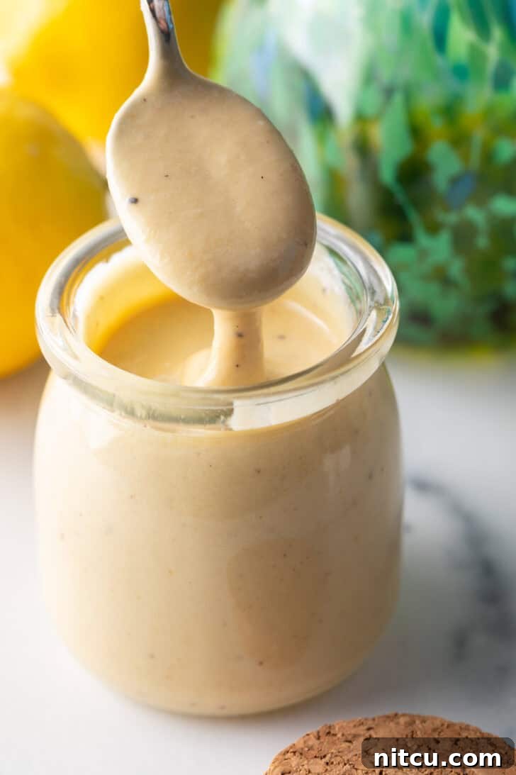 A spoon overflowing with creamy tahini dressing, held above a jar of the same dressing.