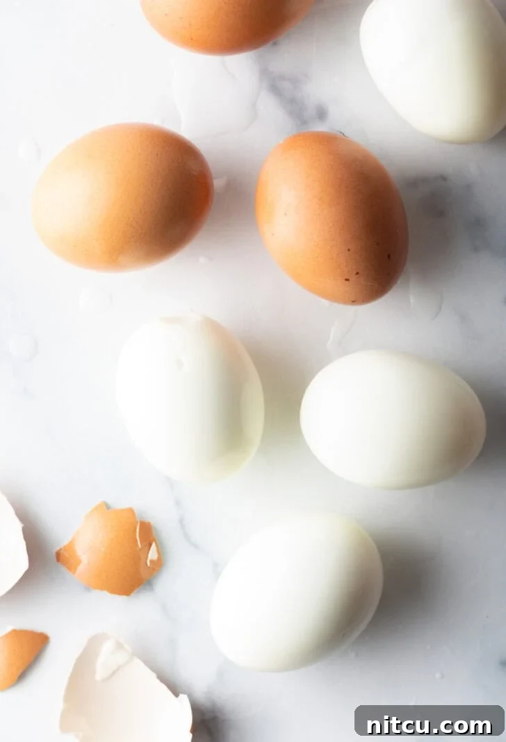 Top down view, four peeled hard boiled eggs and three brown unpeeled eggs.
