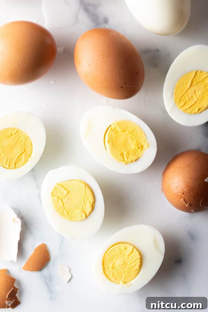A dozen hard boiled eggs on a white marble backdrop. There are five egg halves, four brown eggs in the shell, and one white peeled egg.