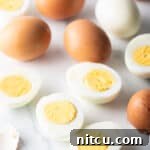 A dozen hard boiled eggs on a white marble backdrop. There are five egg halves, four brown eggs in the shell, and one white peeled egg.