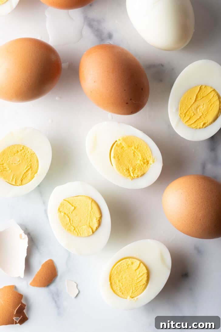 A dozen hard boiled eggs on a white marble backdrop. There are five egg halves, four brown eggs in the shell, and one white peeled egg.