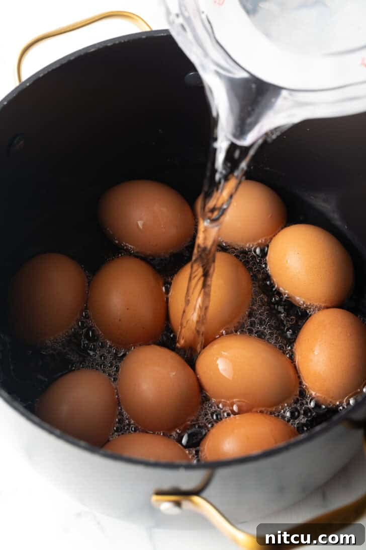 Pouring water from a glass measuring glass over a dozen brown eggs in a black cooking pot.