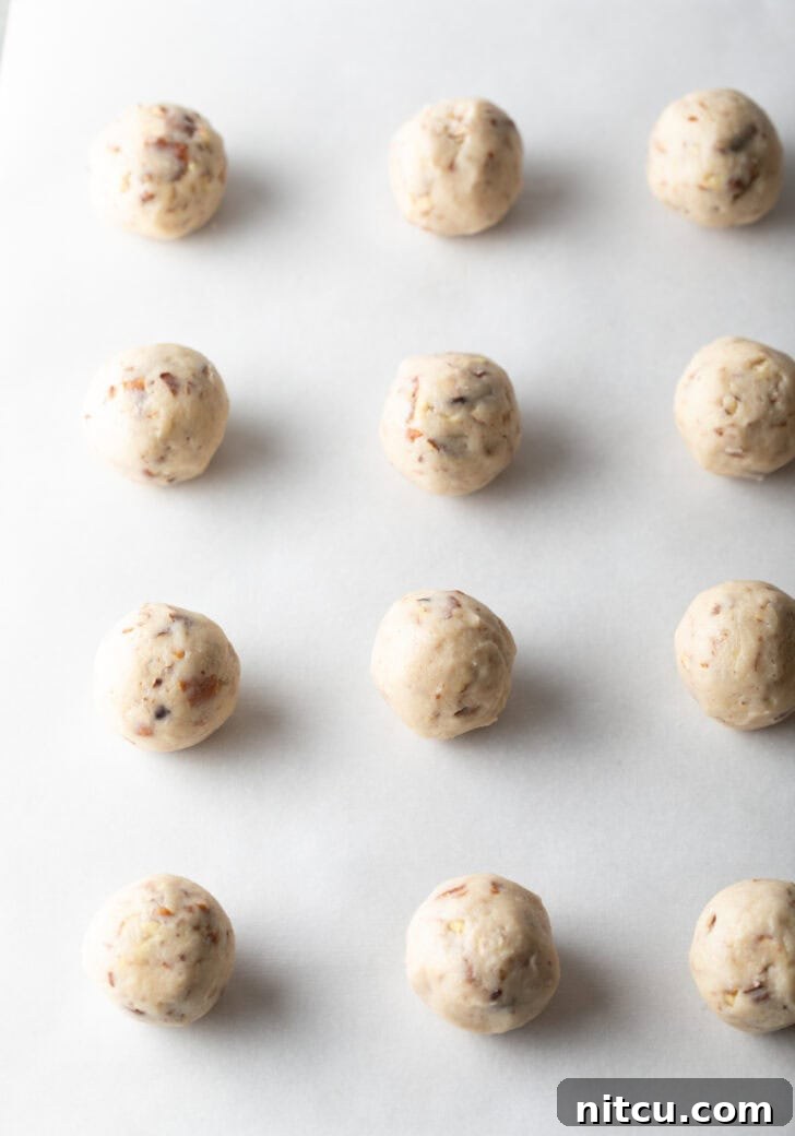 A dozen round balls of cookie dough on a baking sheet.
