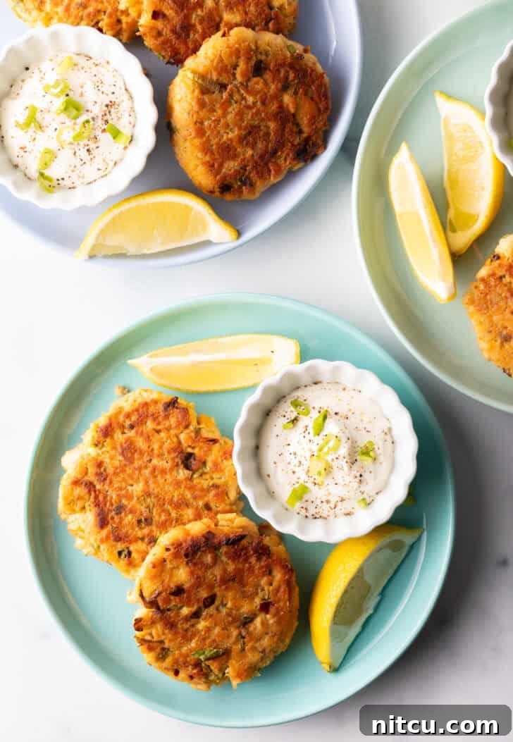 Effortless Golden Salmon Cakes 3 Two perfectly cooked salmon patties on a rustic green plate, garnished with a side of creamy tartar sauce in a white ramekin and fresh lemon wedges, ready to be served.