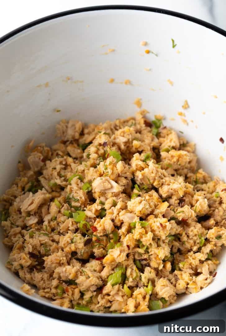 Effortless Golden Salmon Cakes 6 A close-up shot of flaked salmon combined with crushed crackers and freshly chopped herbs in a white mixing bowl, showcasing the texture before forming patties.