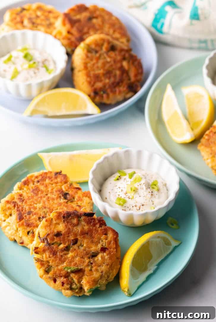 Effortless Golden Salmon Cakes 8 A beautifully arranged serving of old-fashioned salmon patties on a green plate, complete with a ramekin of creamy tartar sauce and fresh lemon wedges.