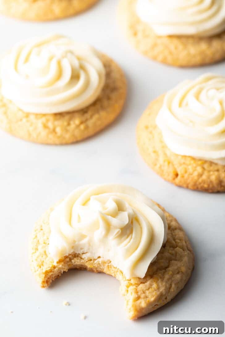 Honey Butter Cornbread Delights 11 Several honey butter cornbread cookies on a white background, each topped with piped frosting. The cookie closest to camera has a bite taken out.