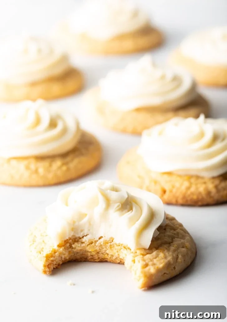 Honey Butter Cornbread Delights 5 Several honey butter cornbread cookies on a white background, each topped with piped frosting. The cookie closest to camera has a bite taken out.