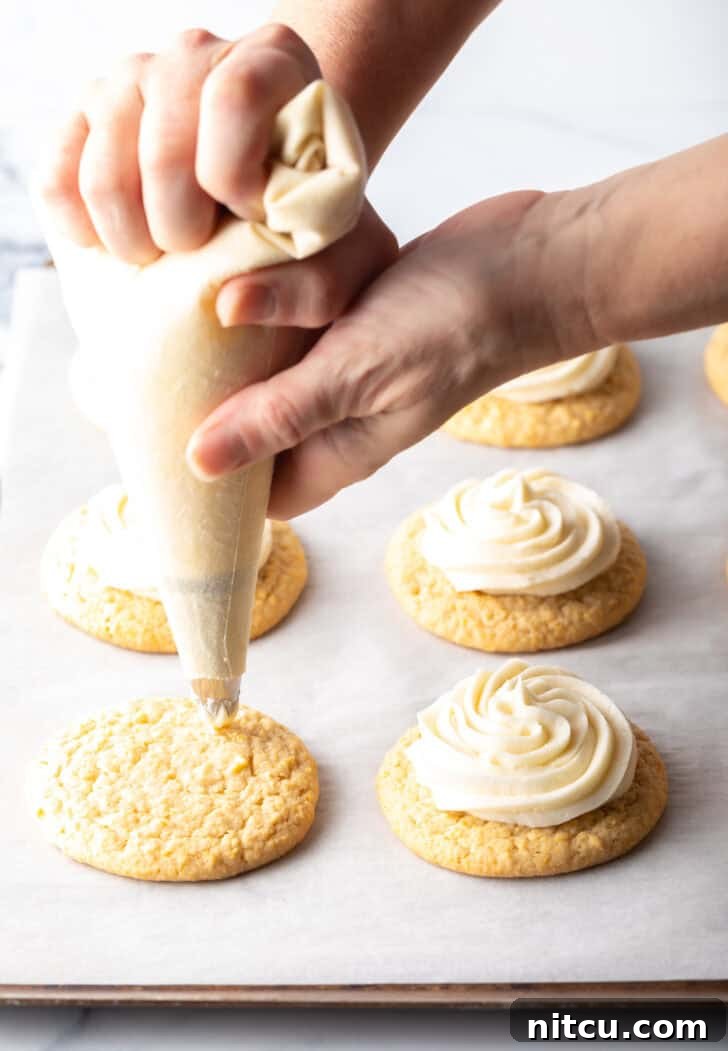Honey Butter Cornbread Delights 9 Hand with a piping bag piping white frosting onto the top of a cornbread cookie.