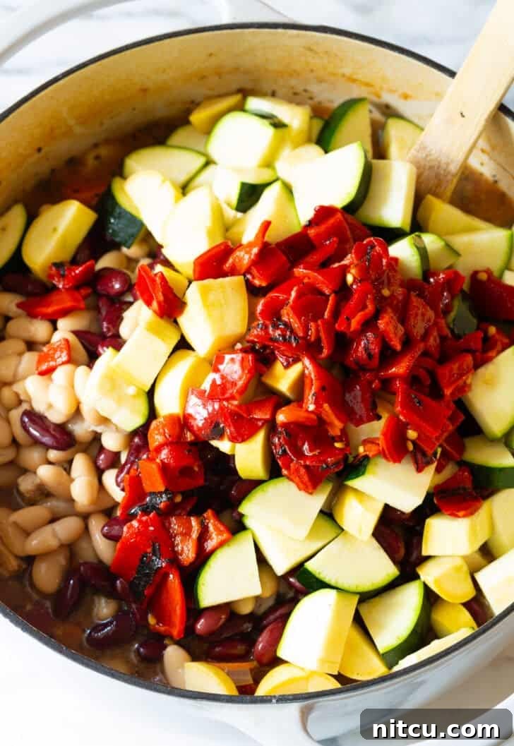 Adding expertly chopped roasted red peppers to a simmering pot filled with zucchini and carrots for a colorful minestrone.