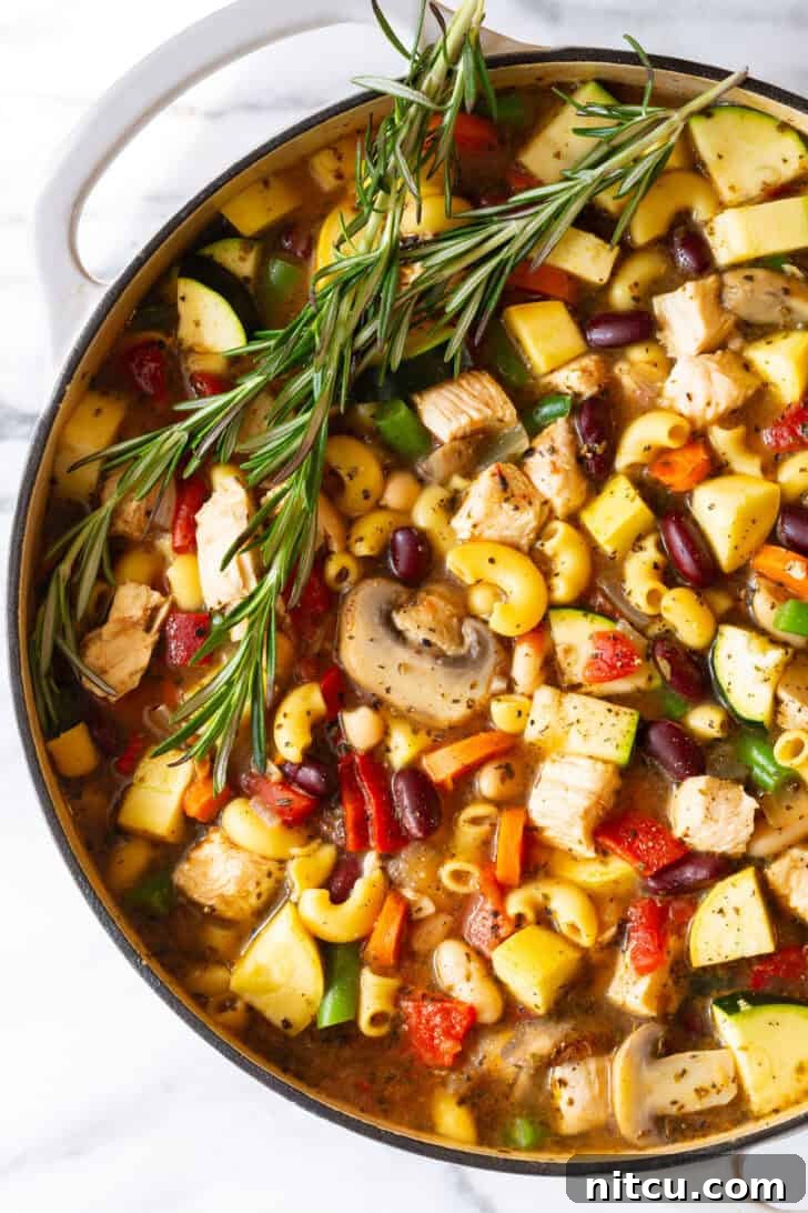 A beautifully presented white pot brimming with homemade chicken minestrone soup, garnished with vibrant sprigs of fresh rosemary, inviting you to a warm meal.
