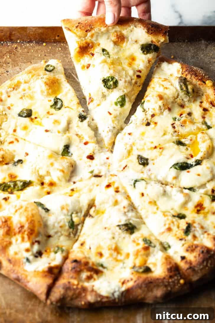 Homemade White Pizza Perfection 13 Pizza with white sauce cut into 8 slices. A hand is removing one slice of pizza from the tray.