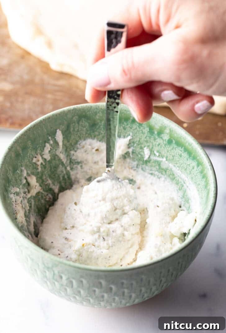 Homemade White Pizza Perfection 6 A hand stirring white sauce ingredients in a green bowl with a spoon.