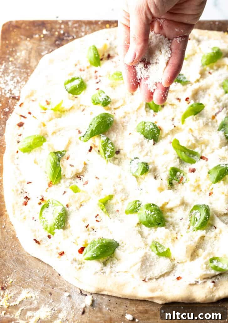 Homemade White Pizza Perfection 9 A hand adding shredded mozzarella cheese on top of the unbaked white pizza.