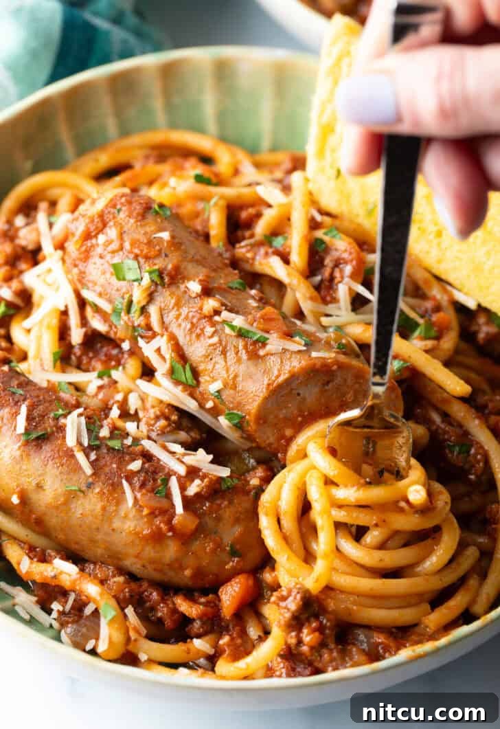 Slow-Simmered Sunday Meat Sauce 12 Hand swirling pasta onto a fork from a green bowl of spaghetti and sausage pasta.