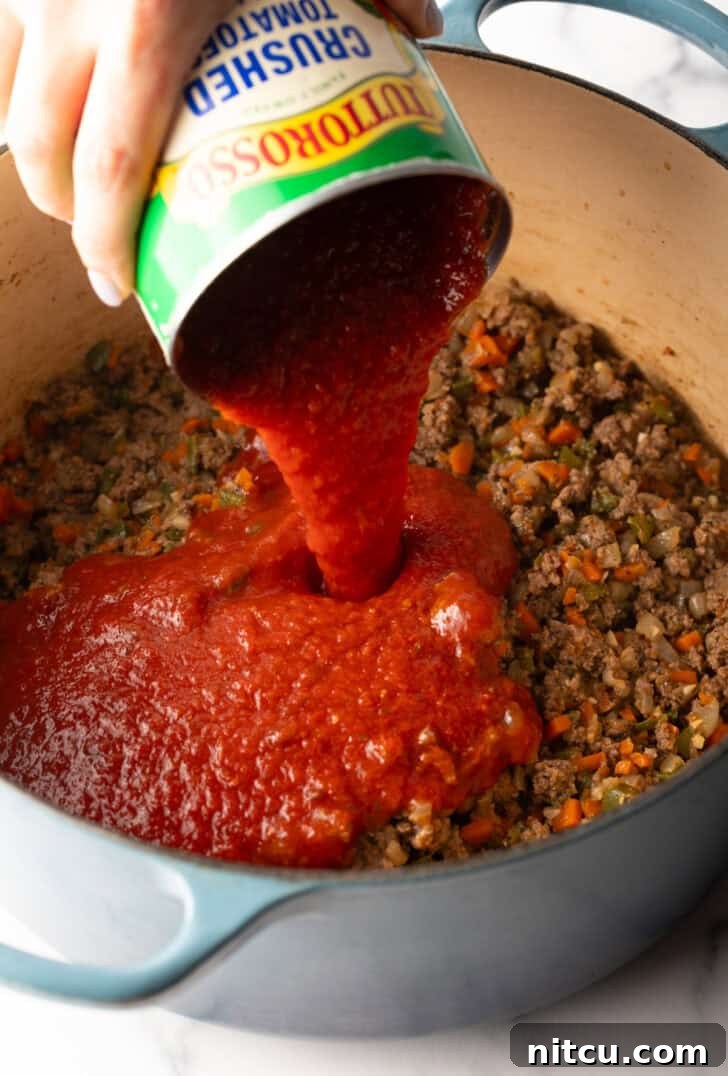 Slow-Simmered Sunday Meat Sauce 7 Adding canned tomato sauce to a pot with browned meat and veggies.