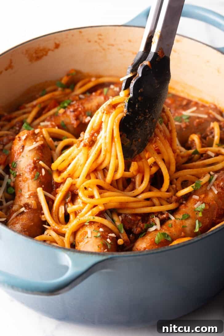 Slow-Simmered Sunday Meat Sauce 9 Tongs taking a serving of pasta from one pot of spaghetti, sausage, and tomato sauce.