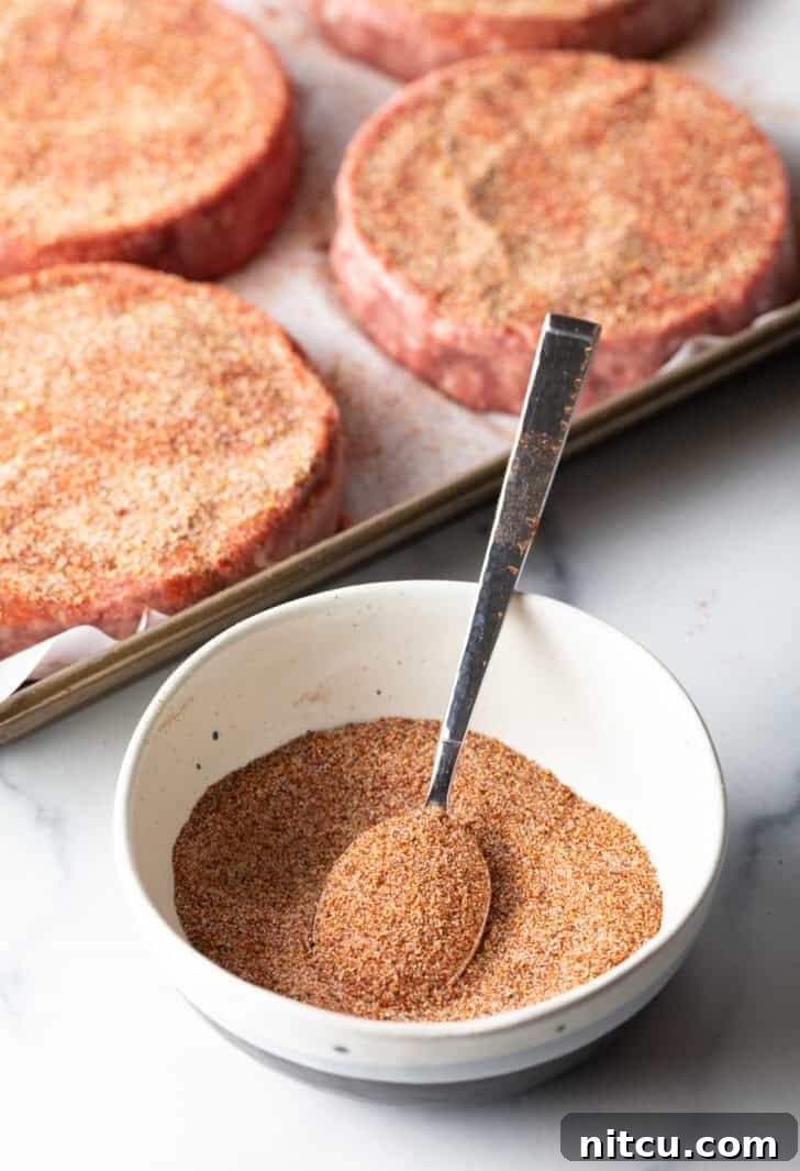 The Ultimate Homemade Burger Spice Blend 2 A white bowl brimming with a vibrant blend of homemade burger seasoning, with a spoon resting beside it, ready to infuse flavor.