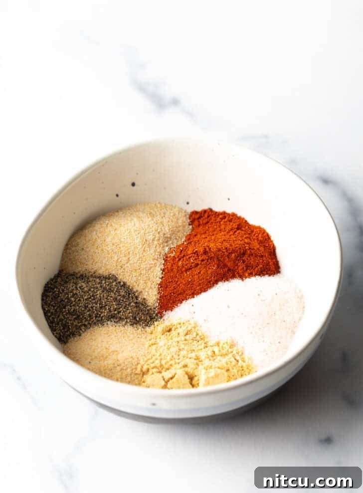 The Ultimate Homemade Burger Spice Blend 5 Separate, neatly arranged piles of smoked paprika, salt, onion powder, black pepper, garlic powder, ground mustard, and a small pinch of cayenne pepper in a white bowl, ready to be mixed.