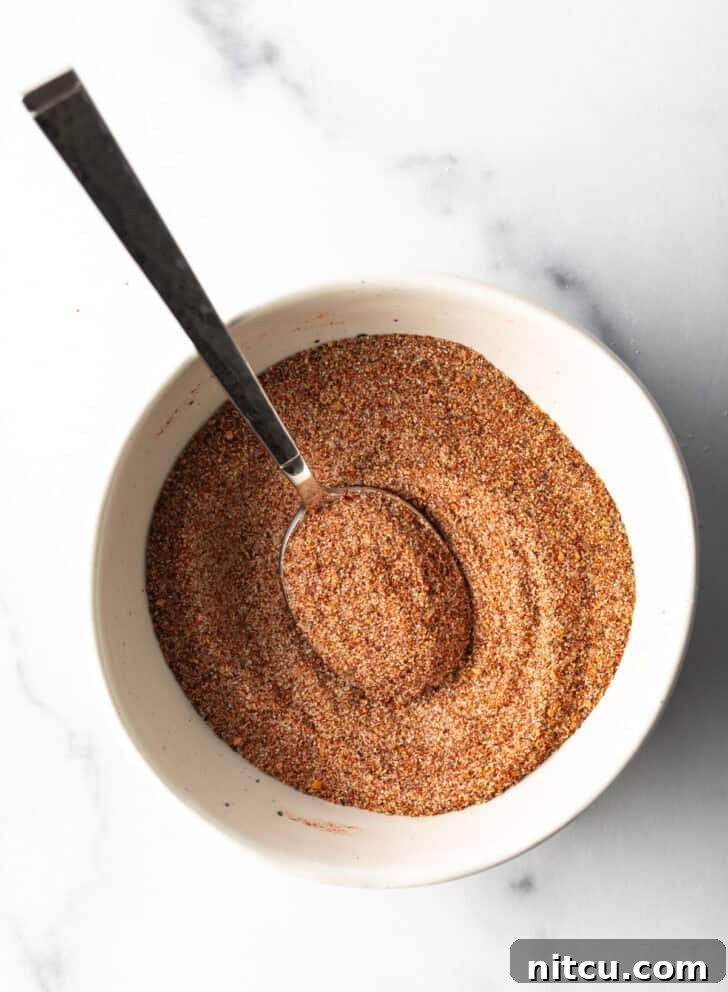 The Ultimate Homemade Burger Spice Blend 7 Top-down view of a white bowl filled with the mixed burger seasoning, with a spoon nestled within the spices.