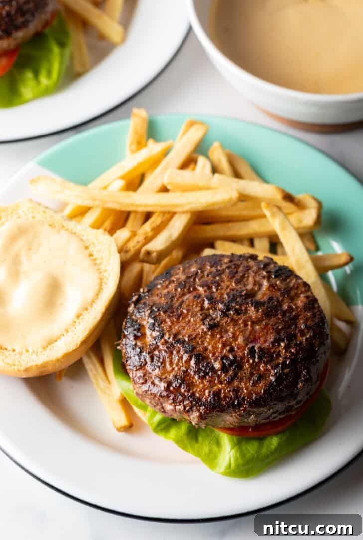 The Ultimate Homemade Burger Spice Blend 10 An open-faced burger showcasing its juicy patty and toppings, presented on a plate with crispy french fries.
