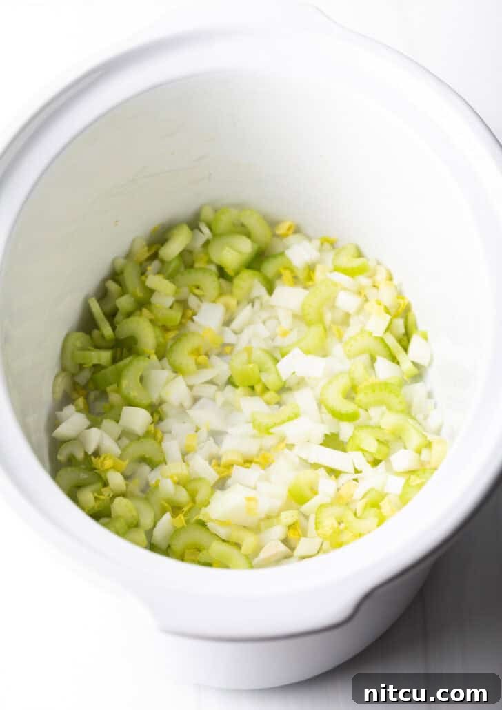 Chopped celery and onion layered in the bottom of a white slow cooker.