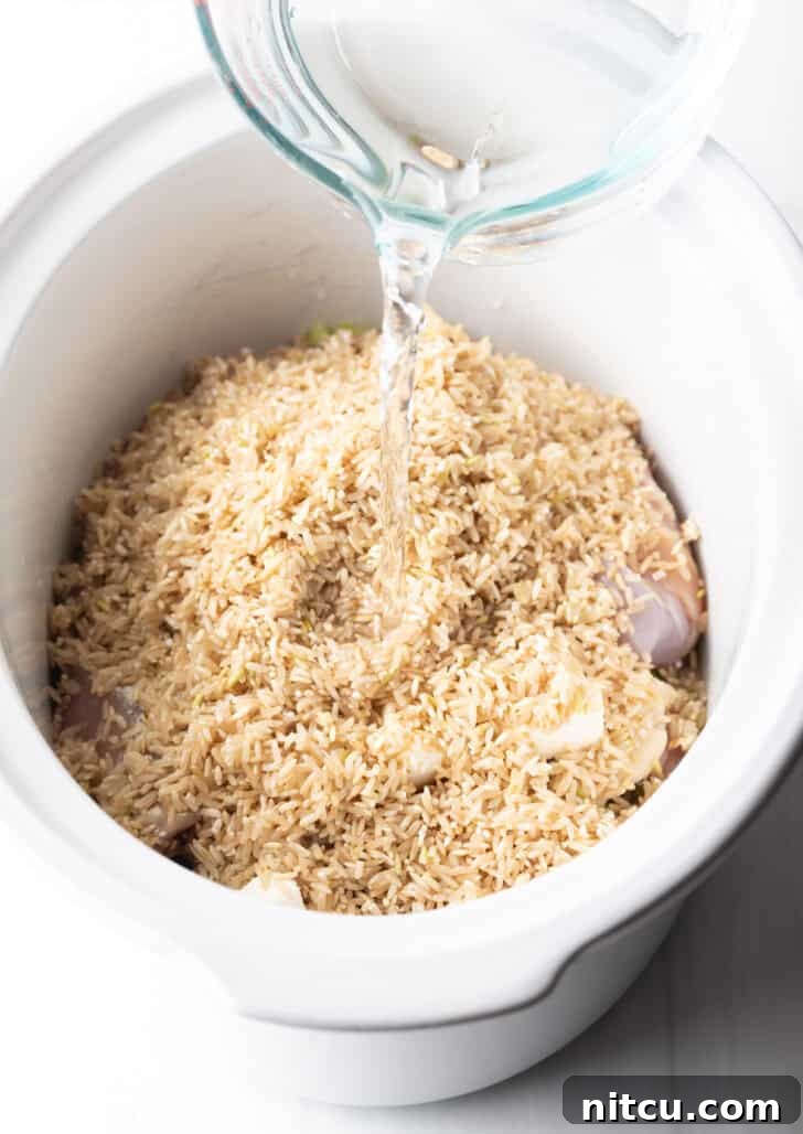 Pouring water into a slow cooker containing chicken thighs and brown rice.