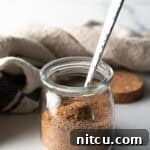 Small glass jar with pork chop seasoning and a metal spoon.