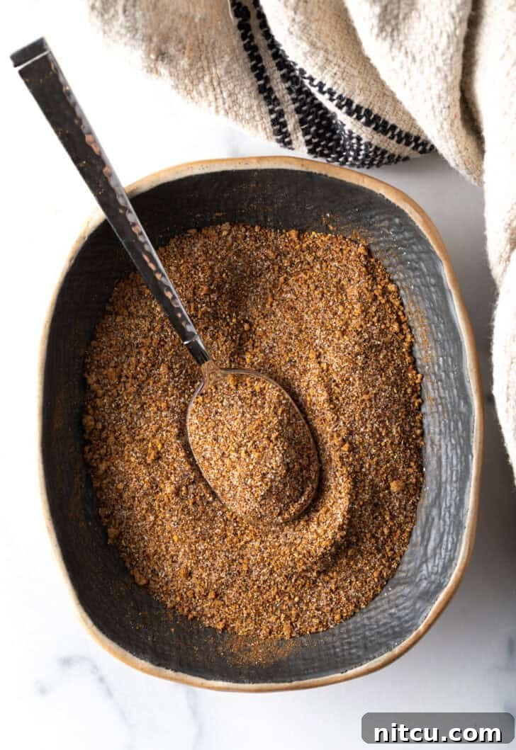 Signature Pork Chop Seasoning 4 Top down view of a blend of spices in an oval dish with a metal spoon, showcasing the rich colors.