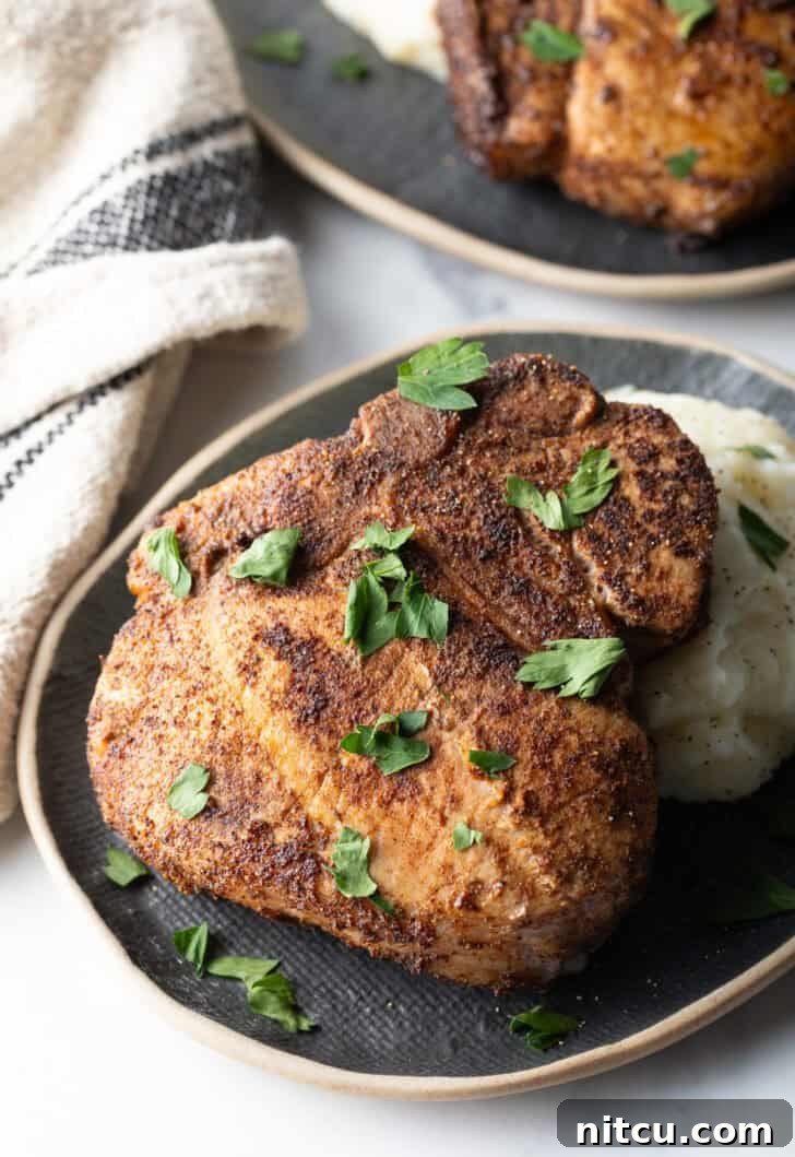 Signature Pork Chop Seasoning 5 Browned seasoned bone-in pork chop on a plate with mashed potatoes, garnished with chopped parsley, ready to be served.