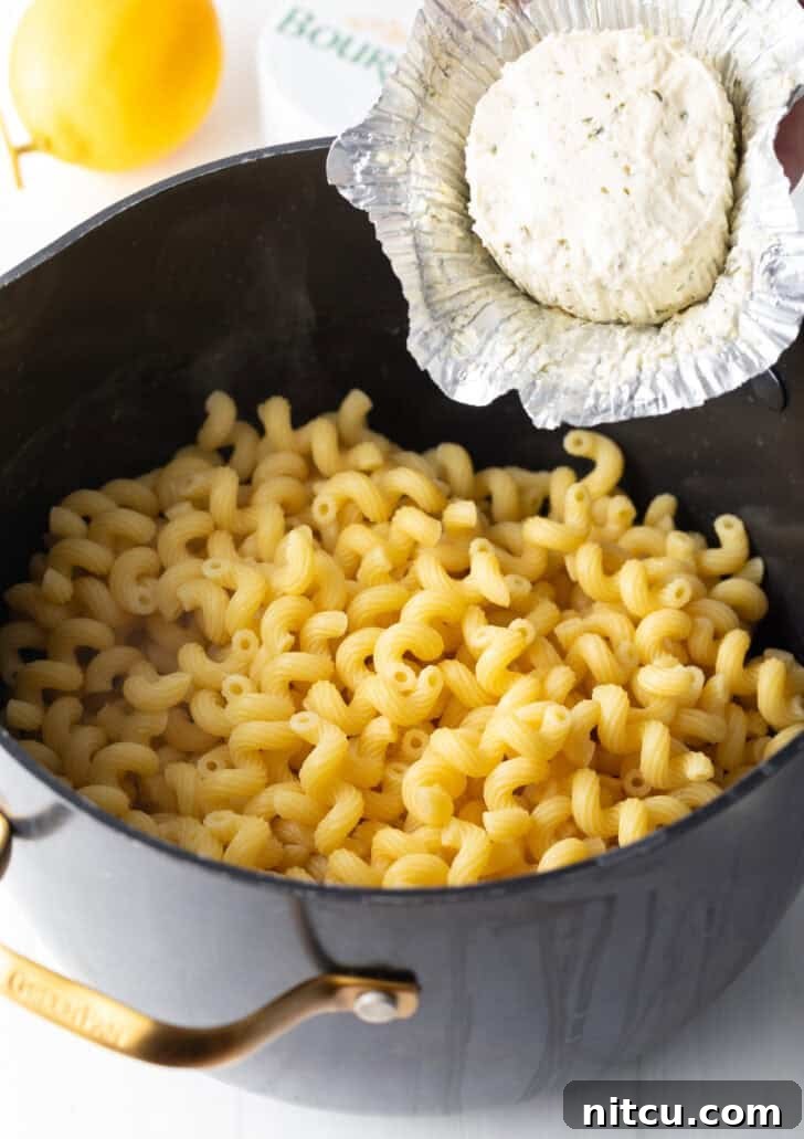 Decadent Boursin Pasta 6 Adding creamy Boursin cheese directly from its wrapper into a pot of freshly cooked macaroni noodles.