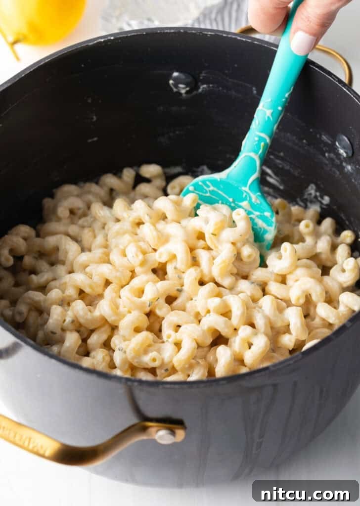 Decadent Boursin Pasta 8 A hand stirring pasta and a rich cheese sauce in a large pot using a blue spatula, ensuring every noodle is coated.