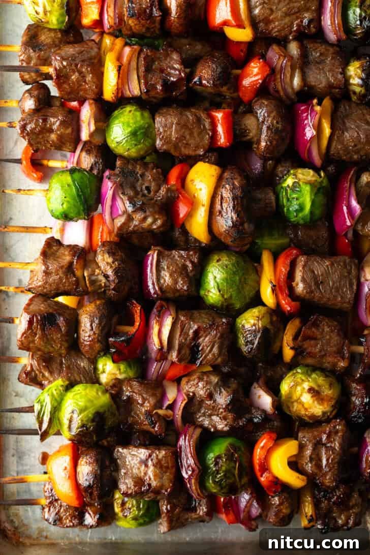 An appetizing top-down view of a dozen perfectly grilled beef and vegetable kabobs arranged neatly.
