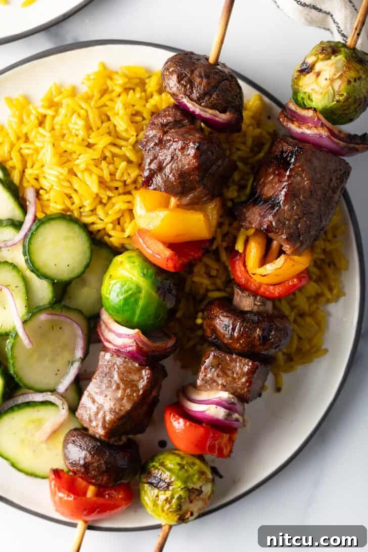 A final, appetizing shot of a white plate with two beef and veggie kabobs, accompanied by yellow rice and a refreshing cucumber salad, ready to be enjoyed.
