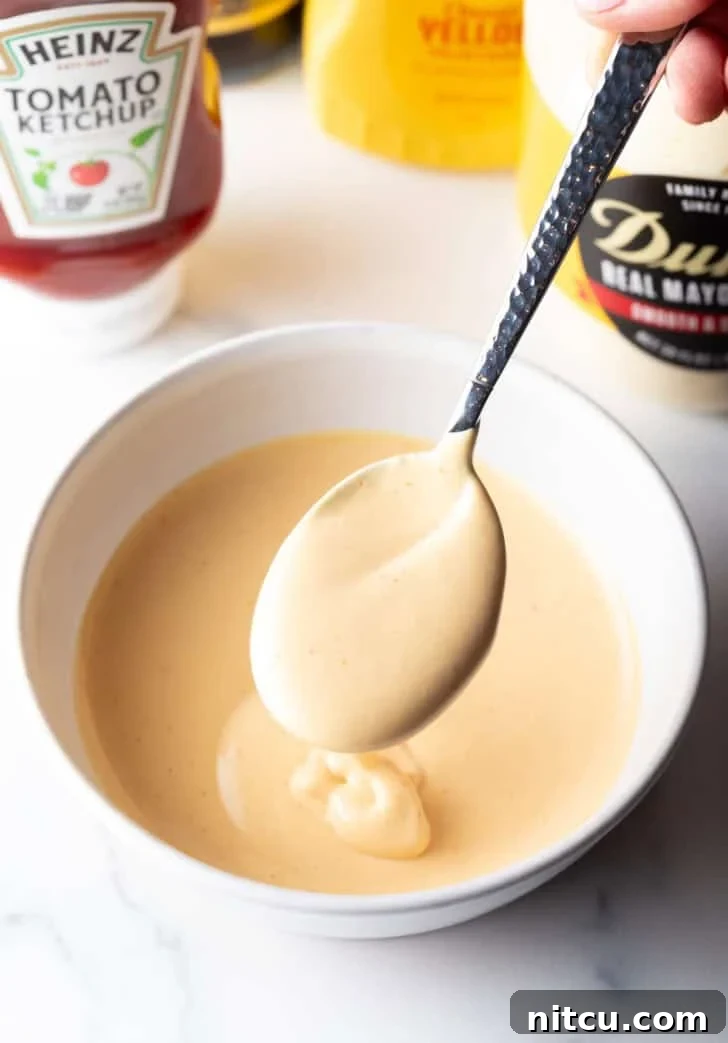 Signature Burger Dressing 2 A spoon full of homemade burger sauce is held over a bowl of the creamy condiment, ready to be served.