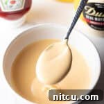 A spoon full of homemade burger sauce is held over a bowl of the creamy condiment.