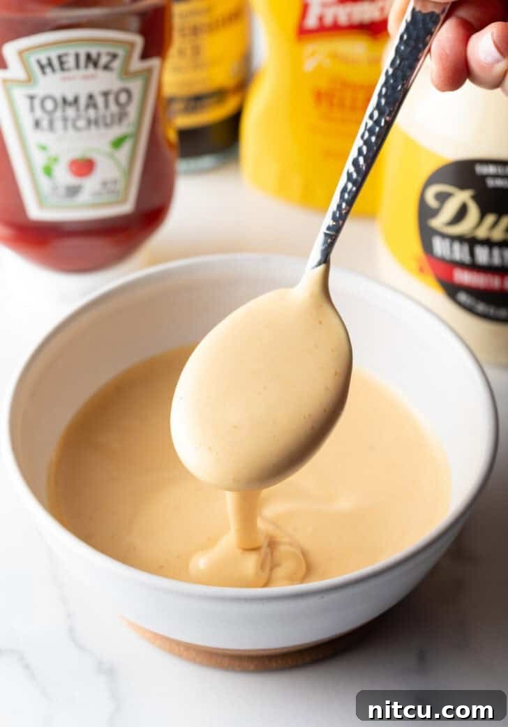 Signature Burger Dressing 8 A spoonful of burger sauce is gracefully lifted over a bowl of the freshly made condiment, showcasing its creamy texture.