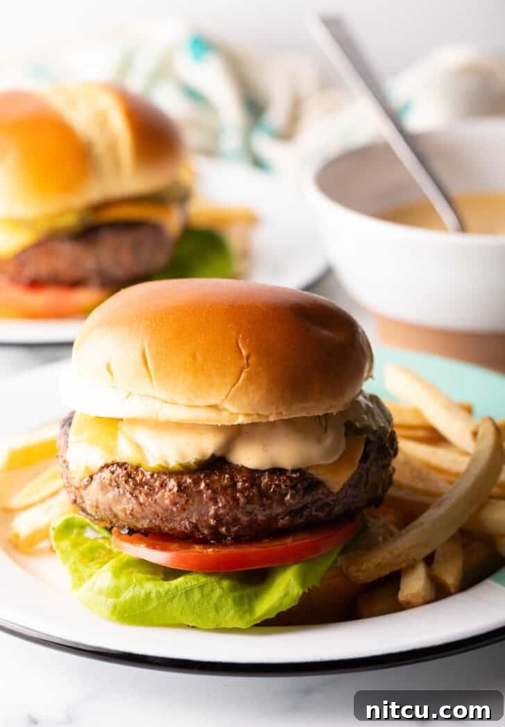 Signature Burger Dressing 9 A mouthwatering cheeseburger, complete with fresh lettuce, ripe tomato slices, melted cheese, and a generous layer of homemade Burger King-style sauce. It's elegantly presented on a white plate with a side of golden french fries.