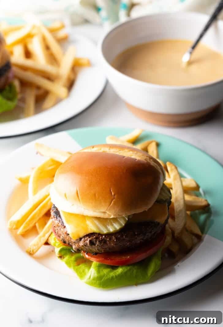 Signature Burger Dressing 10 A close-up of a perfectly constructed cheeseburger, featuring fresh lettuce, juicy tomato, melted cheese, and a generous application of homemade burger sauce, presented on a white plate.