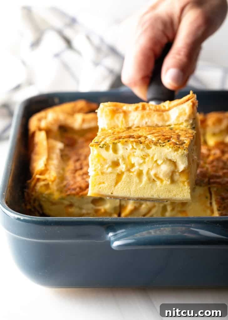 The Ultimate Effortless Breakfast Bake 2 Hand carefully removing a perfectly baked square of golden egg casserole with a spatula from a square baking dish.