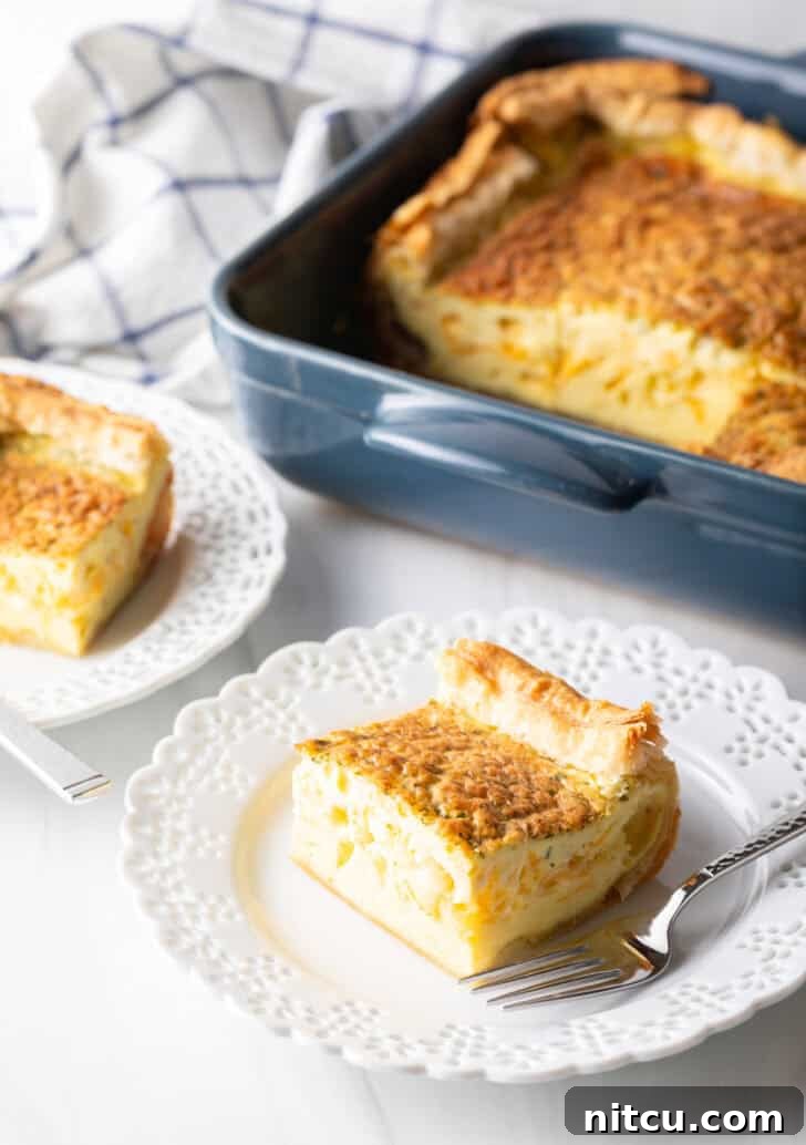 The Ultimate Effortless Breakfast Bake 12 A delightful square of egg casserole sits proudly on a white plate with a fork, while the baking dish with the remaining casserole waits patiently in the soft-focus background.