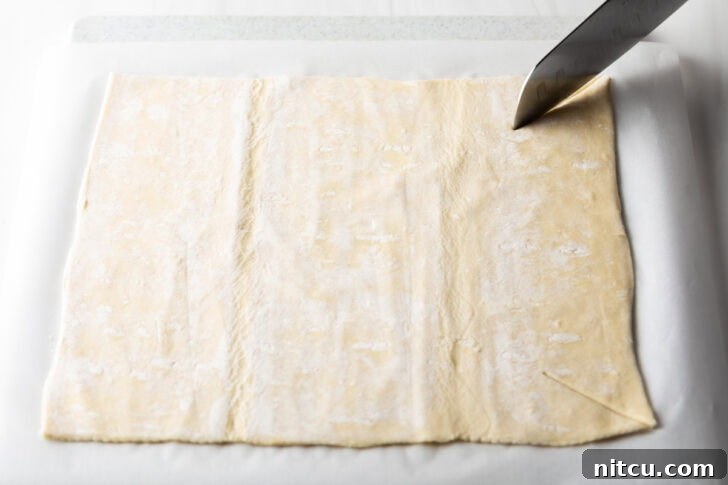The Ultimate Effortless Breakfast Bake 6 Using a sharp knife to carefully slice a large rectangle of puff pastry to the correct dimensions for the baking dish.