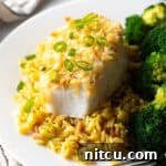 Potato chip crusted and baked bass on a plate with yellow rice and cooked broccoli.