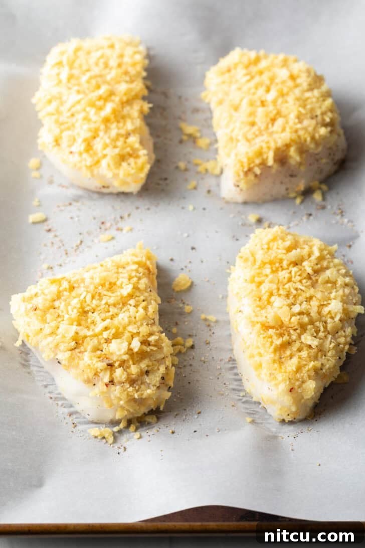 Four beautifully baked fish fillets, perfectly coated in golden-brown crushed potato chips, resting on a baking sheet lined with parchment paper, fresh from the oven.