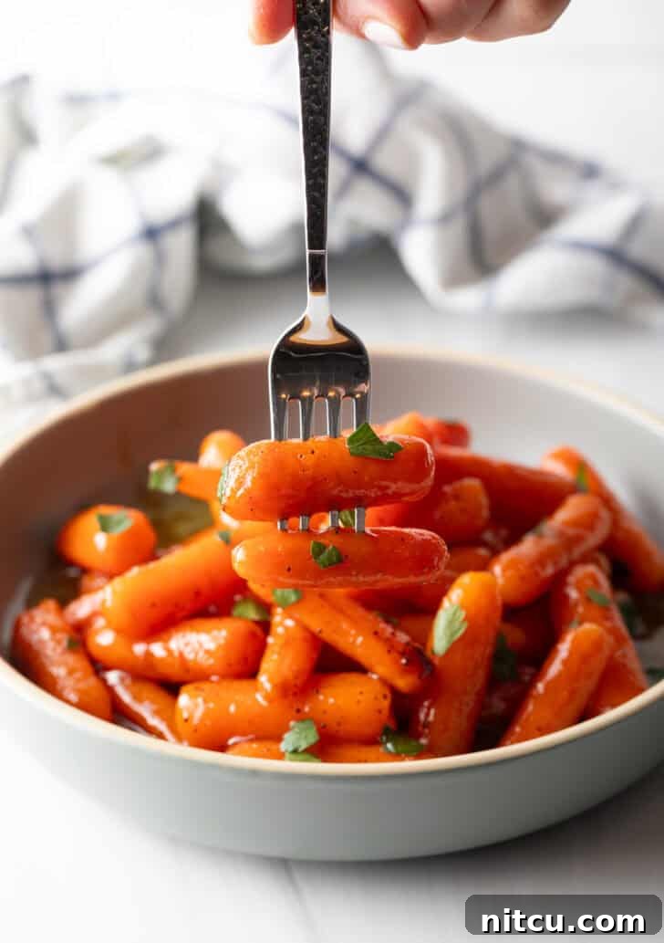 A fork is taking several roasted baby carrots out of a bowl.